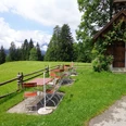 Biergarten Gschwandtnerbauer Holzbänke auf Wiese neben kleiner Kapelle vor Bergkulisse unter leicht bewölktem Himmel