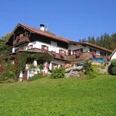 Pfeiffer Alm Alpenhaus mit blumengeschmückten Balkonen, kleiner Kapelle und Auto an sonnigem Hang