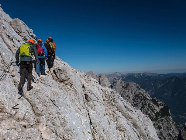 Nordwandsteig Vier Menschen gehen am steilen Fels. Du siehst sie mit Kletterausrüstung.
