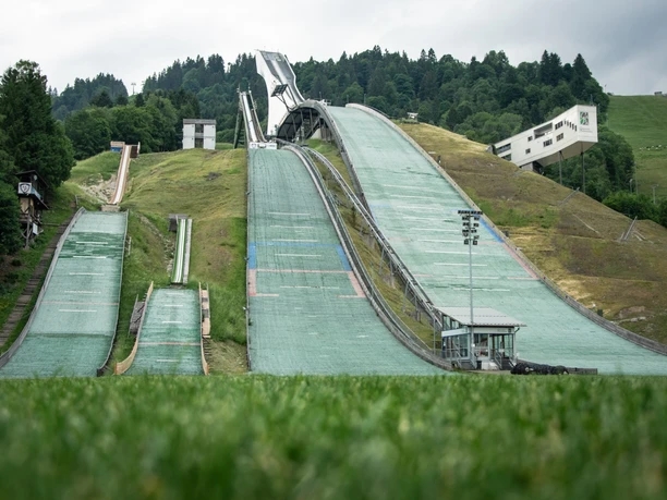 Olympia Skistadion Du siehst große Ski-Hänge für Sprung vor Wald und eine Hütte.