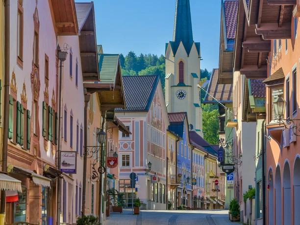 Ludwigstraße Partenkirchen Du siehst eine ruhige Straße mit bunten Häusern und einem hohen Kirchturm.