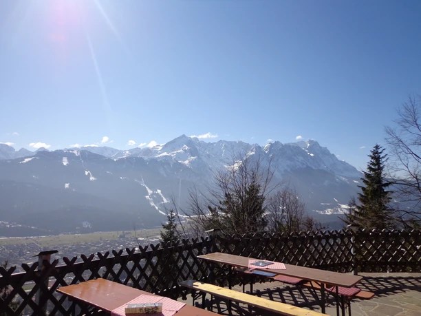 Blick von St. Martin Schneebedeckte Berge über einem Tal, gesehen von einer Terrasse mit Holzbänken und Zaun