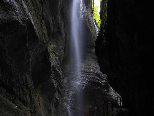 Partnachklamm Schmaler Felsspalt mit herabfallendem Wasser und einem dunklen Steg am rauschenden Bach.