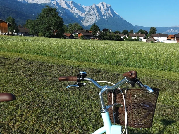 Blick auf das Alpspitz-, Zugspitzgebirge Fahrrad vor Wiese und Dorf mit markanten Bergen unter klarem Himmel