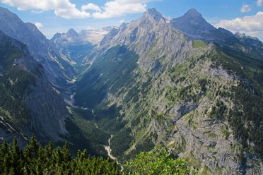 Blick ins Reintal Weitläufiges Bergtal mit steilen Felswänden und bewaldeten Hängen unter blauem Himmel.