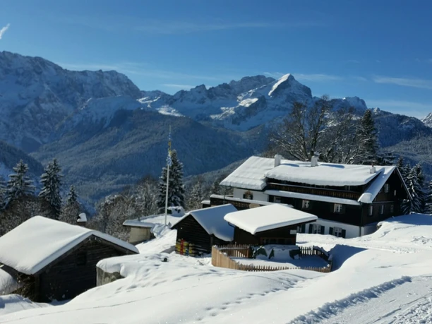 Berggasthof Eckbauer Du siehst einen verschneiten Berggasthof vor hohen Bergen.