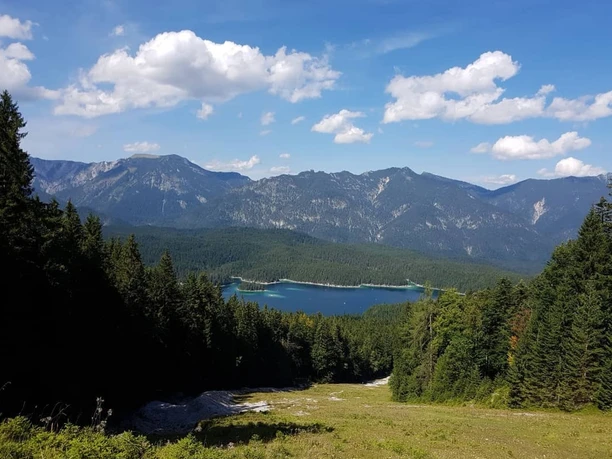 Blick auf den Eibsee Weitläufiger Blick über Waldhänge auf den türkisfarbenen Eibsee vor einer Bergkulisse.