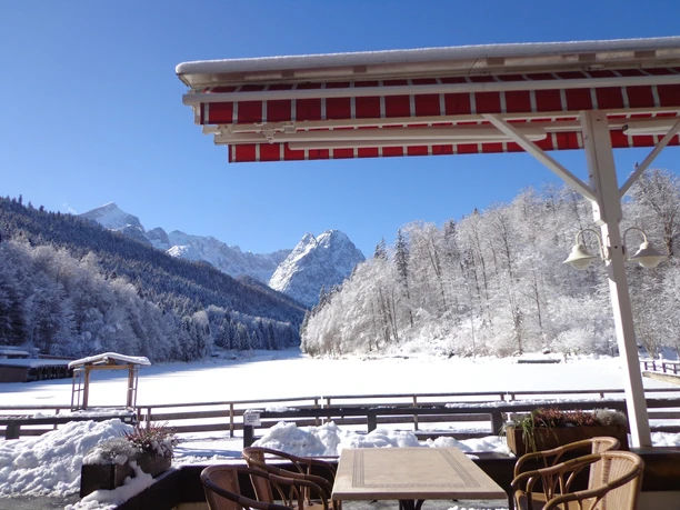 Blick von der Seeterasse Winterliche Terrasse mit Blick auf verschneiten See, umliegende Wälder und Berge.
