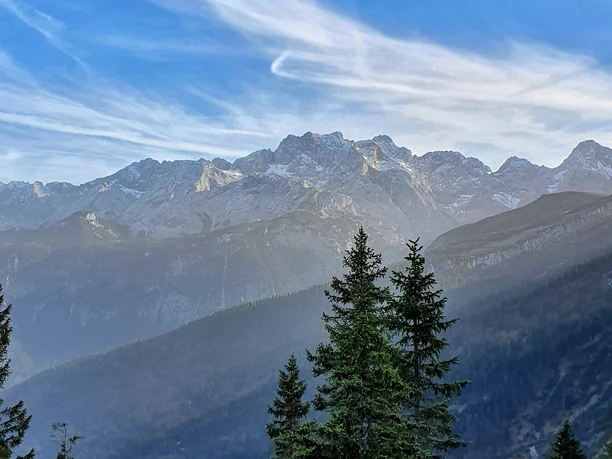 Bergpanorama Blick auf hohe Bergkette über dunklen Waldhängen unter blauem Himmel mit Schleierwolken