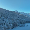 Riessersee Verschneiter Waldhang mit gefrorenem See und sonnenbeschienenen Bergen unter klarem Himmel