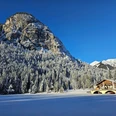 Berggasthof Pflegersee Verschneiter See vor Wald und Felswand mit Berghaus unter klarem Himmel