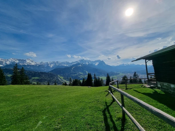 Blick von der Eckenhütte Weitläufige Almfläche mit Holzzaun und Hütte vor schneebedeckten Berggipfeln im Sonnenlicht.