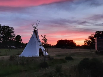 Tipi in Abendstimmung.jpg Ein weißes Tipi steht auf einer Wiese, während der Himmel in kräftigen Abendrot-Tönen leuchtet.