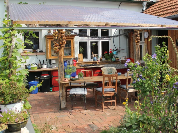 Outdoor-Küche.jpg Covered outdoor kitchen with rustic wooden table, chairs and plants in the garden.