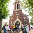 Clara Ernst Platz Gruppe von Menschen steht vor einer Backsteinkirche mit hohem Turm, umgeben von Bäumen im Clara Ernst Platz.