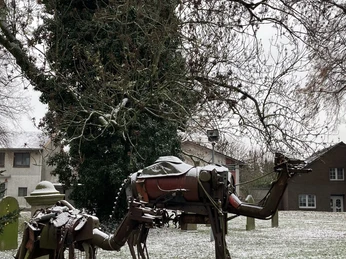 Weihnachtsmarkt Hille Ein Kamel und Reiter aus Metall stehen auf einer verschneiten Wiese, umgeben von Bäumen.