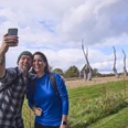 Försterteiche-StaffPark-LTMGmbH-HirschmeierMediaGmbH&CoKG_076.jpg Ein lächelndes Paar macht ein Selfie vor einer Skulpturenlandschaft mit markanten Bäumen.