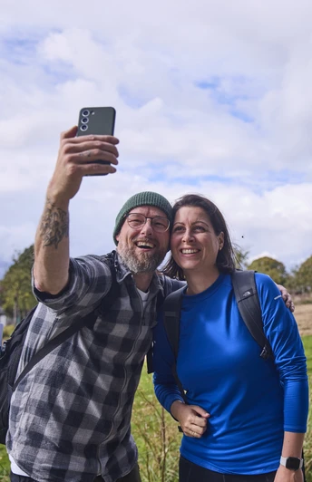 Försterteiche-StaffPark-LTMGmbH-HirschmeierMediaGmbH&CoKG_076.jpg Ein lächelndes Paar macht ein Selfie vor einer Skulpturenlandschaft mit markanten Bäumen.