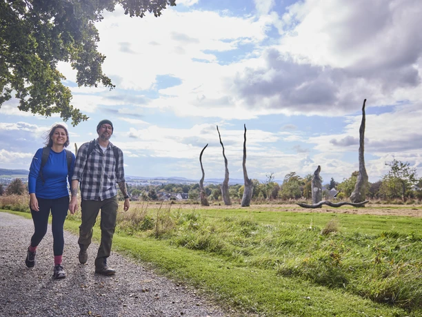 Försterteiche-StaffPark-LTMGmbH-HirschmeierMediaGmbH&CoKG_083.jpg Zwei Personen spazieren auf einem Schotterweg durch eine weitläufige Landschaft mit Skulpturen.
