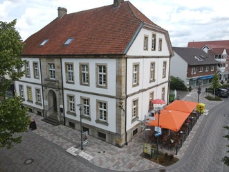 Historisches Gebäude mit roten Ziegeldach und weißen Fassaden, integriertes Straßencafé außen.