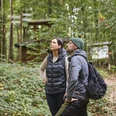 Zwei Personen bestaunen die grüne Waldlandschaft auf einem naturbelassenen Pfad.