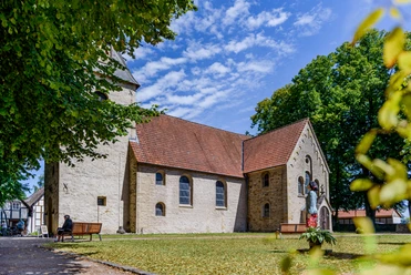 Eine historische Kirche mit roten Dachziegeln, umgeben von Bäumen und einem gepflegten Rasen.