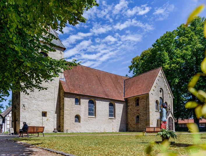 Eine historische Kirche mit roten Dachziegeln, umgeben von Bäumen und einem gepflegten Rasen.