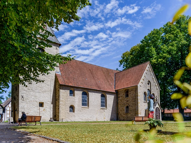 _BBB6910.jpeg Eine historische Kirche mit roten Dachziegeln, umgeben von Bäumen und einem gepflegten Rasen.