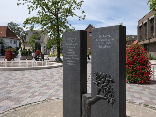 Denkmal jüdische Gemeinde 164 © Markus Stein.jpg Gedenktafel mit Baumrelief in gepflastertem Platz, Fontäne und umliegenden Gebäuden im Hintergrund.