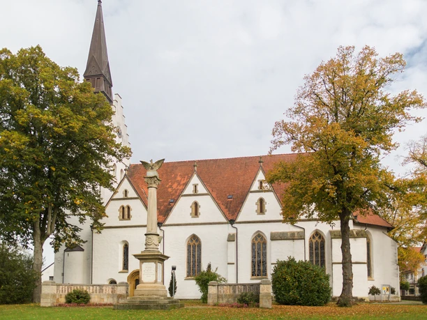St. Petri-Kirche.jpg Eine weiße Kirche mit spitzem Turm, umgeben von Bäumen, im Herbstlaub, vor bewölktem Himmel.