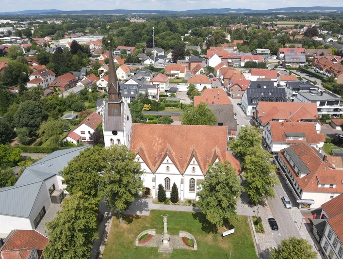 Stadt_Versmold.JPG Luftaufnahme einer Kirche mit rotem Dach, umgeben von Bäumen und Wohnhäusern in einer Stadtlandschaft.