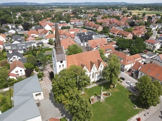 Luftaufnahme einer Kirche in einem Wohngebiet mit roten Dächern und umliegenden Bäumen.