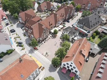 DJI_0459.JPG Luftaufnahme eines malerischen Platzes mit Brunnen, umgeben von Häusern mit roten Dächern und Cafés.