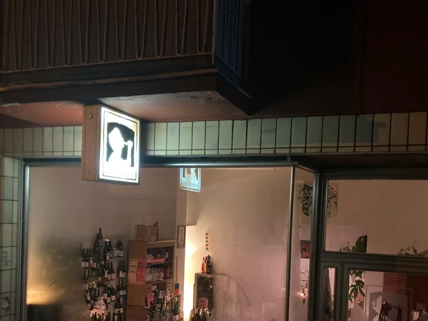 La Vincaillerie Evening scene of a small wine store with illuminated shop windows and many bottles of wine.