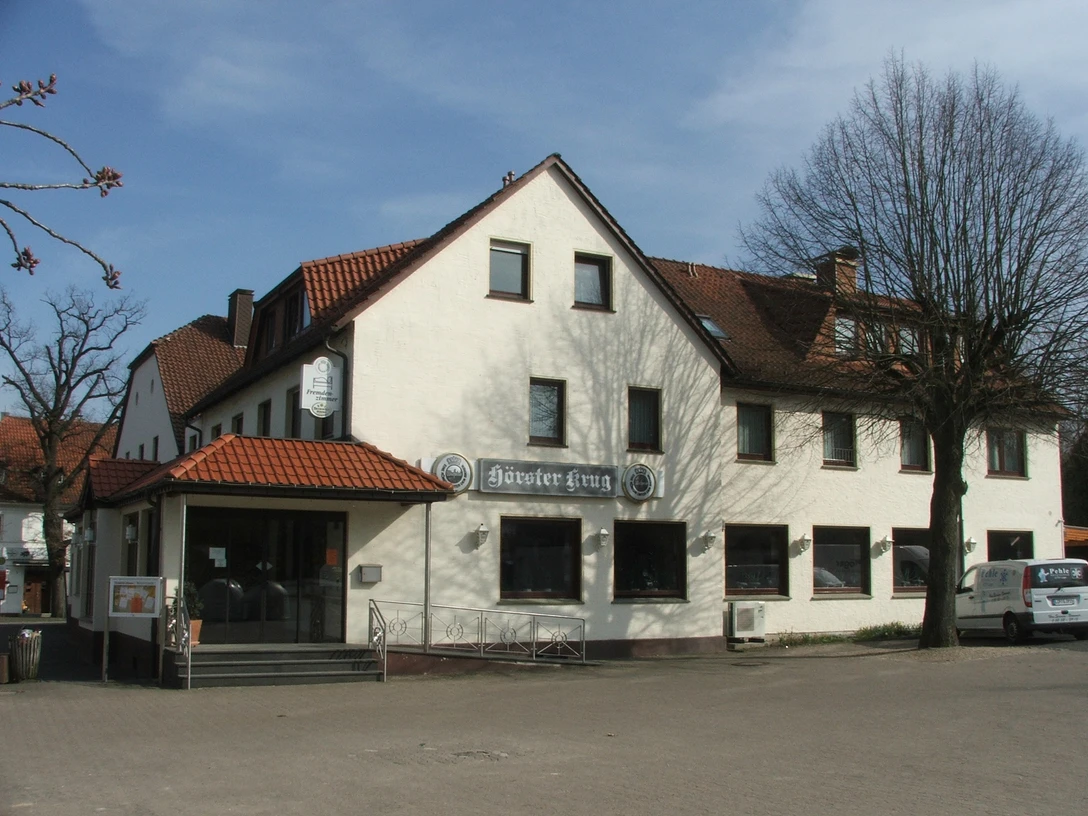 Hörster Krug Ein traditionelles Fachwerkgebäude mit roten Ziegeldächern und weißen Wänden, umgeben von Bäumen.