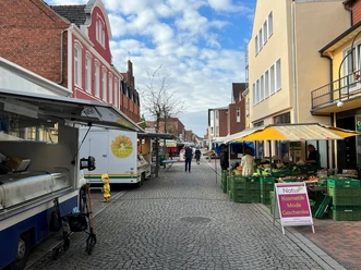 Marktszene in einer gepflasterten Straße mit Ständen voller frischer Produkte und bunten Marktschirmen.