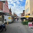 Wochenmarkt Hoya Marktszene in einer gepflasterten Straße mit Ständen voller frischer Produkte und bunten Marktschirmen.