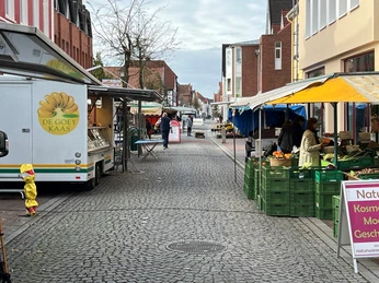 Marktstände entlang einer gepflasterten Straße mit Menschen, die frische Produkte einkaufen.