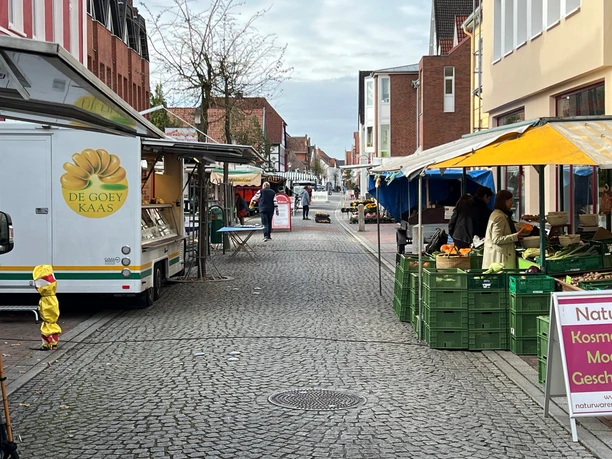 Wochenmarkt Hoya Marktstände entlang einer gepflasterten Straße mit Menschen, die frische Produkte einkaufen.