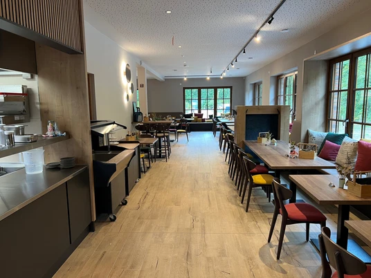 Genusswirtschaft Moderner Gastraum mit Holztischen, bunten Stühlen, großen Fenstern und stilvoller Beleuchtung.Modern dining room with wooden tables, colorful chairs, large windows and stylish lighting.Moderne spisestue med træborde, farverige stole, store vinduer og stilfuld belysning.Moderne eetkamer met houten tafels, kleurrijke stoelen, grote ramen en stijlvolle verlichting.