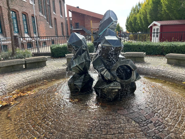 Zwergenbrunnen Moderne skulptur af geometriske former med vandfunktion, placeret på en brolagt plads.