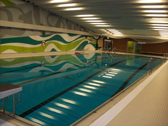 SchwimmWerk Steinhagen 25m-Becken Ein Hallenbad mit blauem Wasser, umgeben von bunten Wänden und einer ruhigen, modernen Atmosphäre.