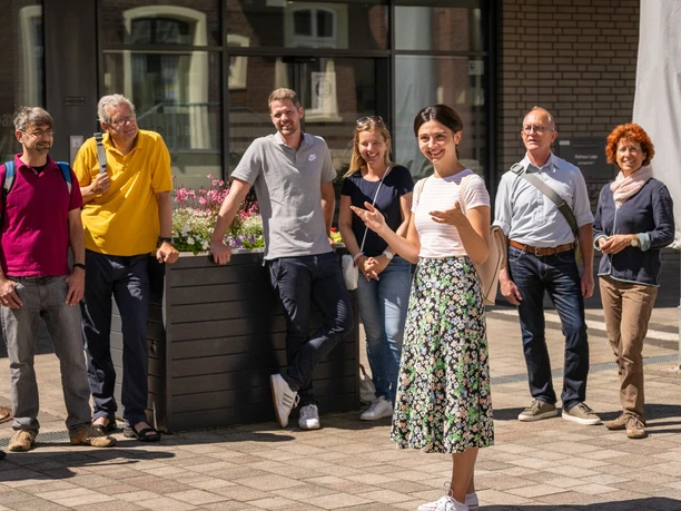 Stadtführung Lage Eine Gruppe von fröhlichen Menschen nimmt an einer informativen Stadtführung bei sonnigem Wetter teil.