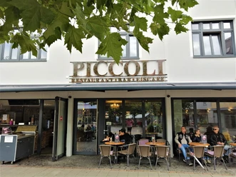 Herford-Piccoli-Aussen-Pro Herford GmbH.jpg Außenansicht des Restaurants Piccoli mit Gästen, die an Tischen vor großen Fenstern sitzen.