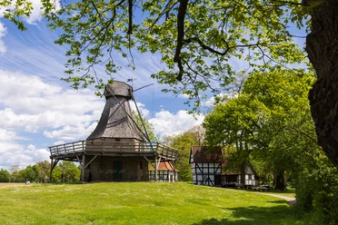 Mühle Levern Die historische Mühle Levern mit Schindeldach liegt malerisch in einer grünen Landschaft unter blauem Himmel.