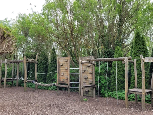 Spielplatz rila erleben Holzspielplatz mit Kletter- und Balanciermöglichkeiten, von Bäumen umgeben, vermittelt Naturerlebnis.
