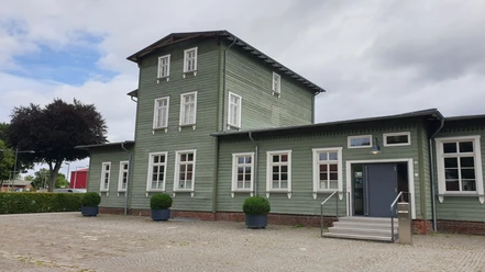 Historischer Bahnhof Rahden mit grüner Holzfassade und symmetrischen weißen Fenstern.