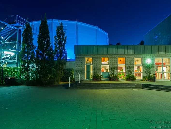 Rietberg_cultura_Günter Rolf_kulturig e.V..jpg Ein beleuchtetes Gebäude bei Nacht mit blauer Kuppel im Hintergrund und Eingangsbereich im Vordergrund.