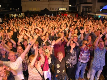 DSC_0721.JPG Das Bild zeigt eine große Menschenmenge bei der Innenstadtfete, die ausgelassen feiert und die Hände in die Luft hebt. Zudem sind viele fröhliche Gesichter und Lichter zu sehen.