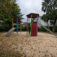Ein moderner Spielplatz mit Klettergerüst, Rutsche und Wipptieren, umgeben von herbstlichem Laub.